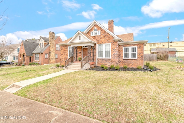 view of front of property with brick siding, fence, roof with shingles, a front lawn, and a chimney