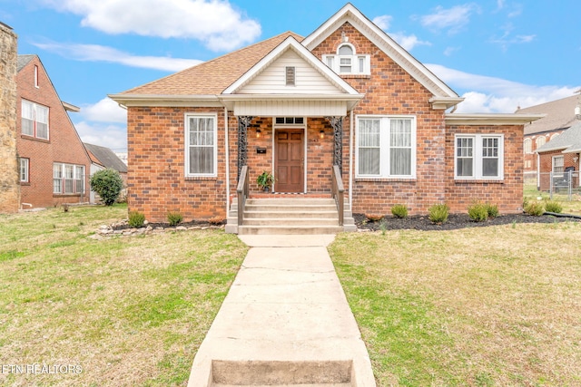 bungalow-style home with a front yard, brick siding, and roof with shingles