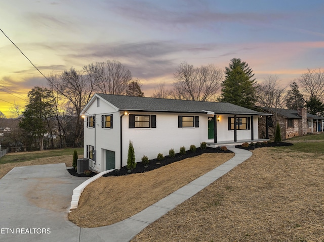 view of front of house featuring a shingled roof, concrete driveway, central AC, and a front yard