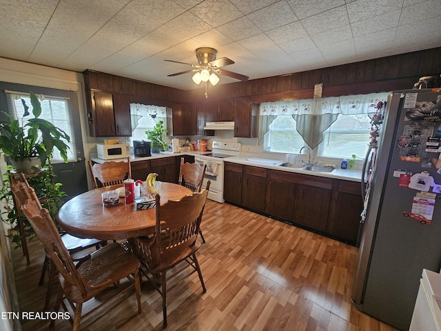 kitchen featuring light countertops, light wood-style floors, a sink, white appliances, and under cabinet range hood