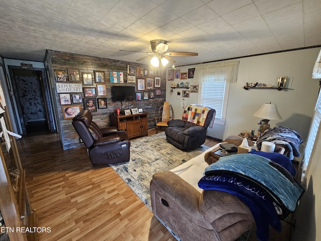 living room with a ceiling fan, an accent wall, and wood finished floors