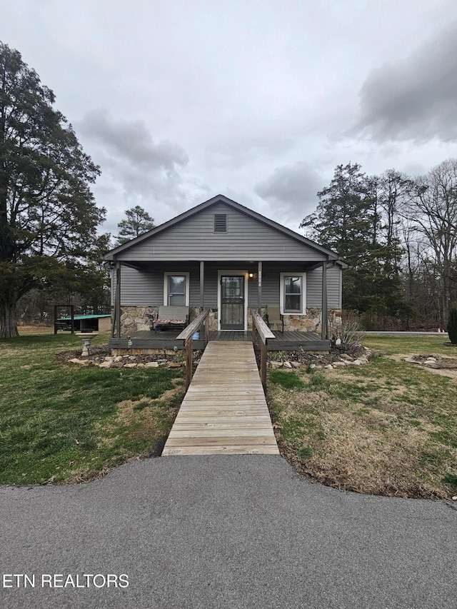 bungalow featuring stone siding, covered porch, and a front lawn