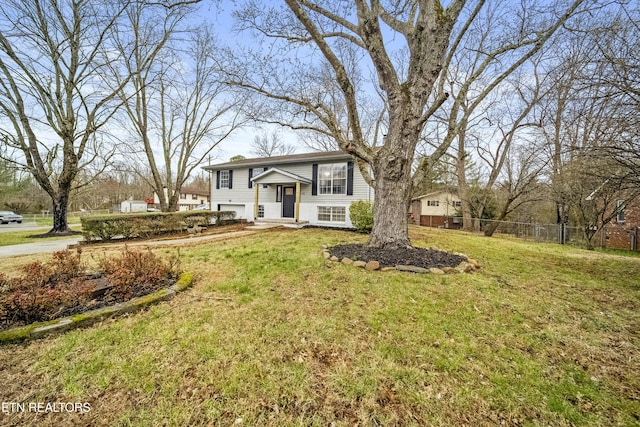 raised ranch with a front yard, fence, and an attached garage