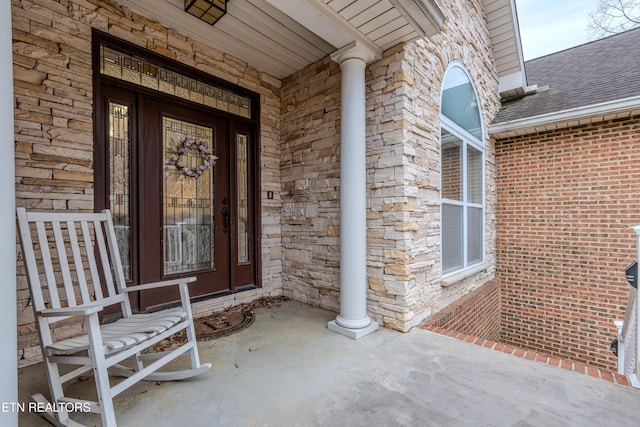 property entrance featuring covered porch, stone siding, brick siding, and roof with shingles