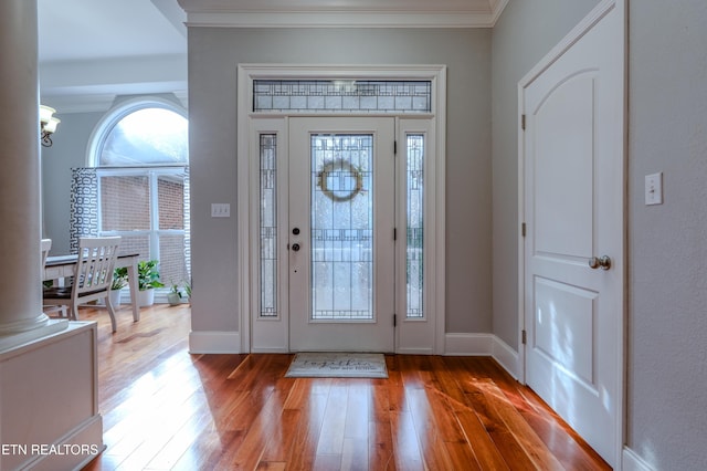 entrance foyer featuring ornamental molding, wood finished floors, decorative columns, and baseboards