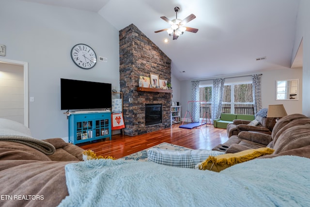 living area with visible vents, ceiling fan, a stone fireplace, wood finished floors, and high vaulted ceiling