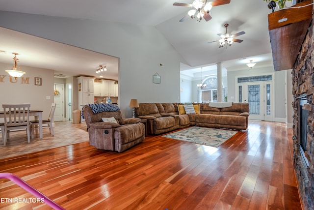 living room featuring light wood finished floors, high vaulted ceiling, a stone fireplace, and ceiling fan with notable chandelier