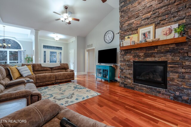 living room with ornamental molding, a stone fireplace, wood finished floors, high vaulted ceiling, and ceiling fan with notable chandelier