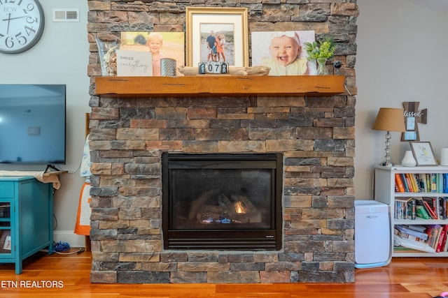 room details with visible vents, a stone fireplace, and wood finished floors