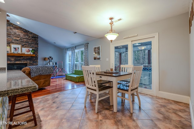 dining room with lofted ceiling, visible vents, a stone fireplace, tile patterned flooring, and baseboards