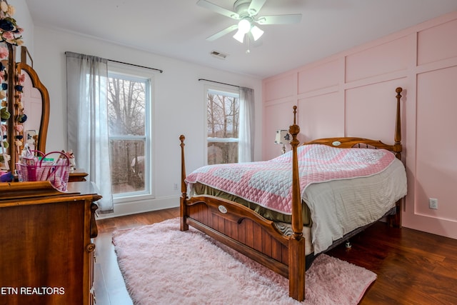 bedroom with a ceiling fan, wood finished floors, visible vents, and a decorative wall