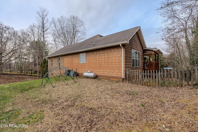 view of side of home with central AC unit, fence, and roof with shingles