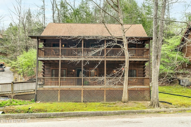 rear view of house featuring a yard, log exterior, a shingled roof, and a porch