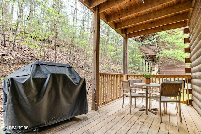 deck featuring outdoor dining area, a view of trees, and area for grilling