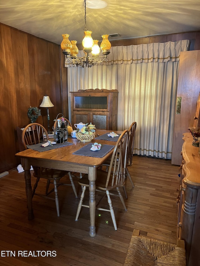 dining area featuring visible vents, a notable chandelier, wooden walls, and wood finished floors