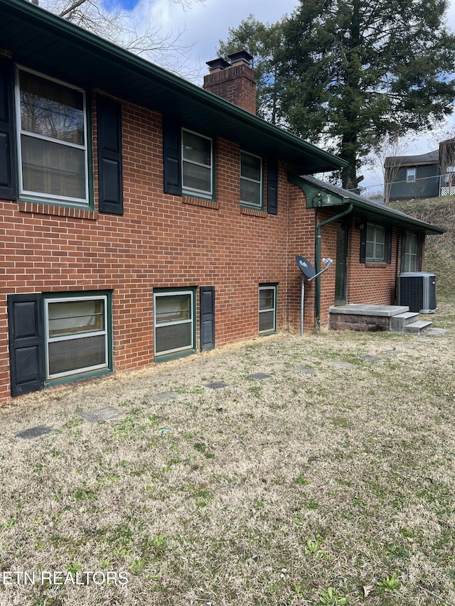 rear view of property with a yard, central AC, brick siding, and a chimney