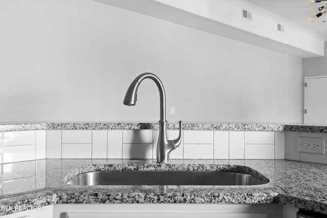 kitchen with a sink, visible vents, and light stone counters