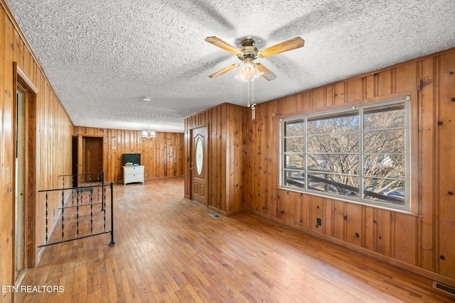 empty room with visible vents, wood-type flooring, a ceiling fan, and wooden walls