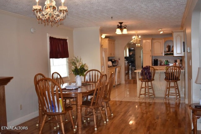 dining space with crown molding, a chandelier, light wood-type flooring, arched walkways, and a textured ceiling