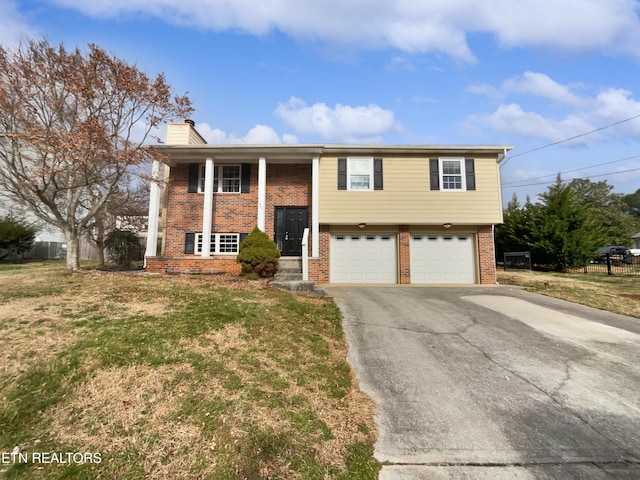 split foyer home featuring brick siding, a chimney, an attached garage, a front yard, and driveway