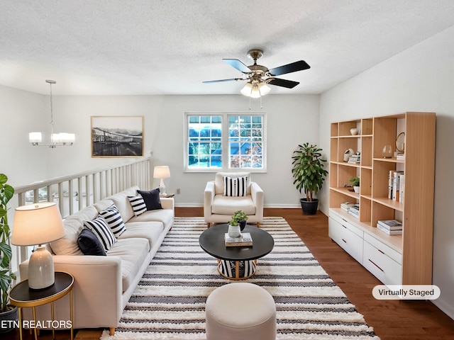 living area featuring a textured ceiling, dark wood-type flooring, ceiling fan with notable chandelier, and baseboards