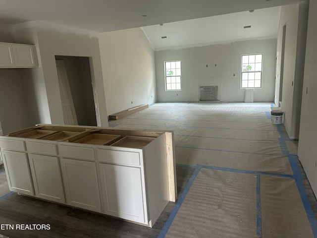 kitchen with vaulted ceiling, white cabinets, a fireplace, and open floor plan