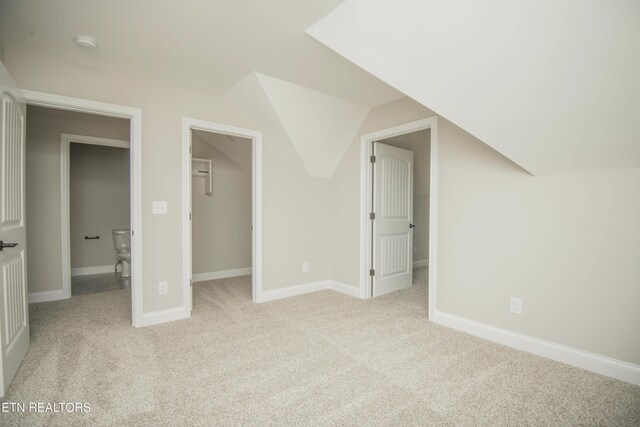 unfurnished bedroom with vaulted ceiling, a closet, light carpet, a walk in closet, and baseboards