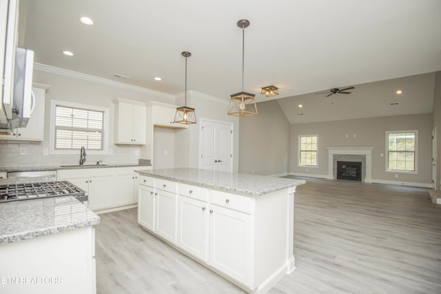 kitchen with a sink, light wood finished floors, tasteful backsplash, hanging light fixtures, and ceiling fan