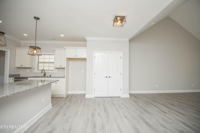 kitchen with tasteful backsplash, light wood-type flooring, hanging light fixtures, a sink, and white cabinets