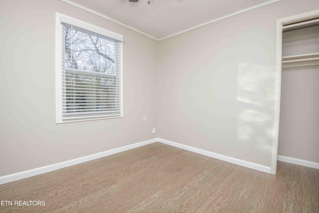 unfurnished bedroom with crown molding, a closet, wood finished floors, and baseboards