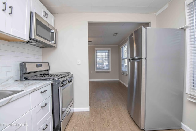 kitchen featuring white cabinets, appliances with stainless steel finishes, light stone counters, light wood-type flooring, and backsplash