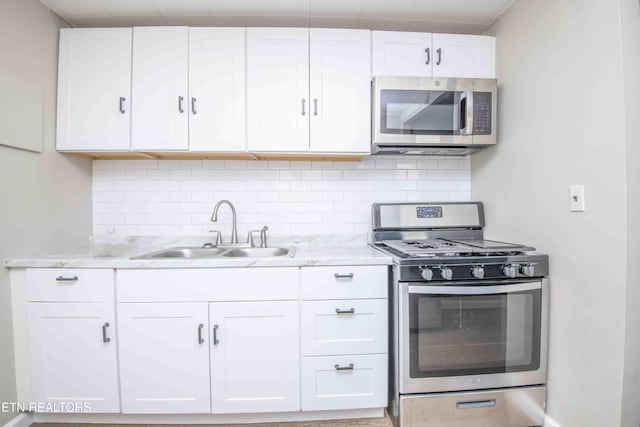 kitchen with appliances with stainless steel finishes, a sink, white cabinets, and tasteful backsplash