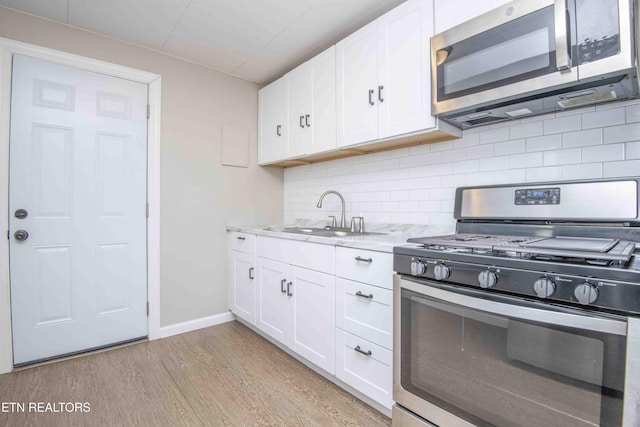 kitchen with white cabinets, a sink, stainless steel appliances, light wood-style floors, and backsplash