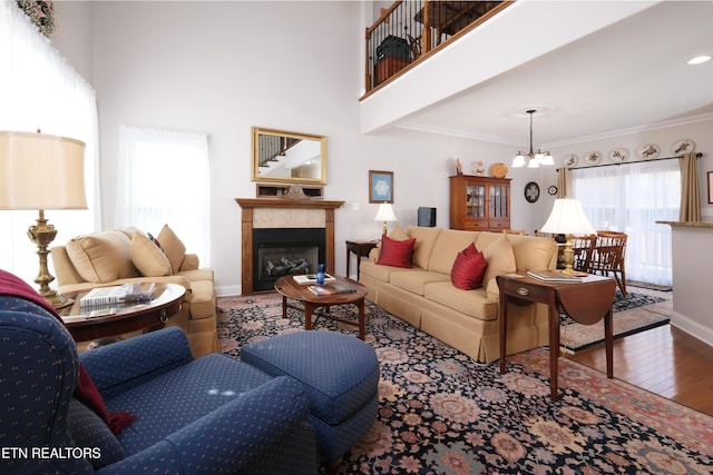 living room featuring a chandelier, hardwood / wood-style flooring, a towering ceiling, baseboards, and ornamental molding