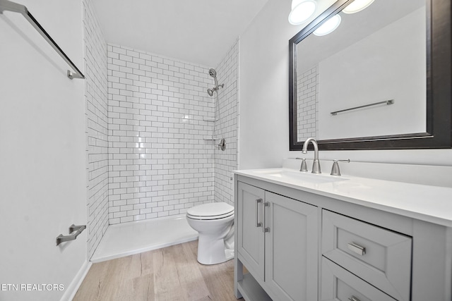 full bath featuring tiled shower, vanity, toilet, and wood finished floors