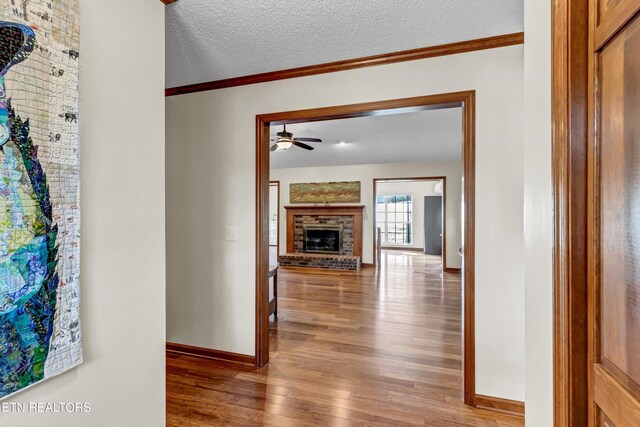 hallway featuring baseboards, a textured ceiling, ornamental molding, and wood finished floors