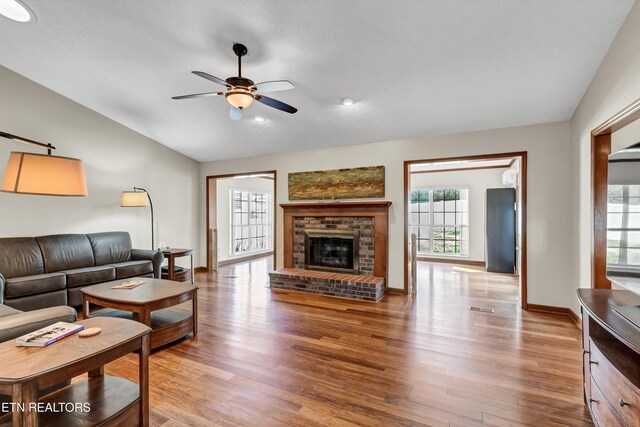 living room with ceiling fan, a fireplace, vaulted ceiling, and wood finished floors