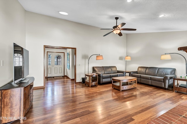 living room featuring dark wood-style floors, ceiling fan, high vaulted ceiling, and baseboards