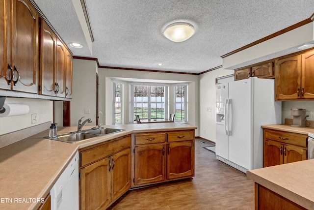 kitchen with white appliances, ornamental molding, a peninsula, light countertops, and a sink