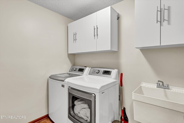 laundry area featuring cabinet space, a sink, a textured ceiling, washer and dryer, and baseboards