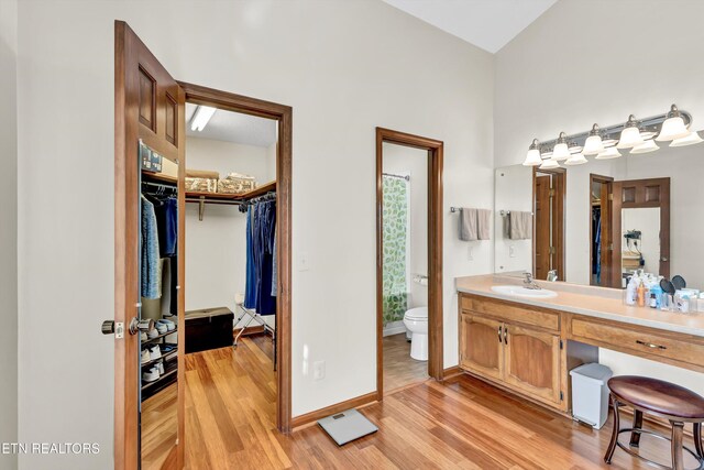 full bathroom featuring toilet, wood finished floors, vanity, baseboards, and a walk in closet