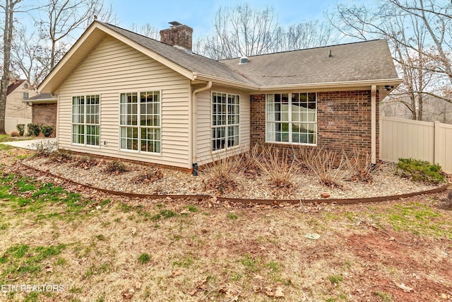 view of side of property featuring roof with shingles, a chimney, fence, and brick siding