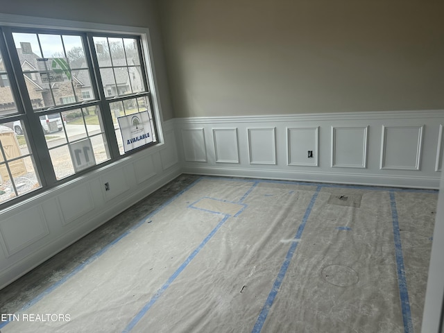 unfurnished room with wainscoting and a decorative wall