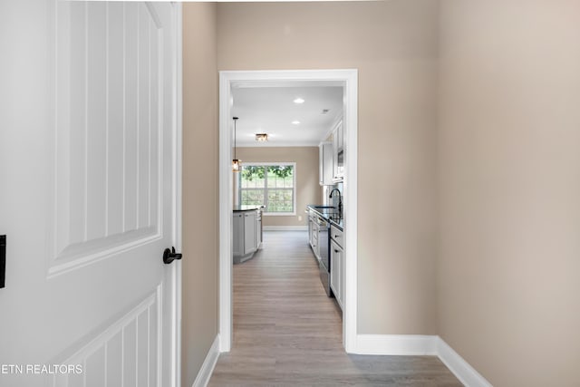 hall featuring baseboards, a sink, recessed lighting, and light wood-type flooring