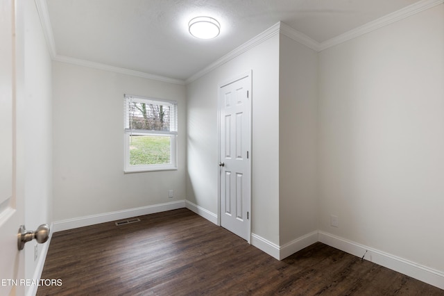 empty room with dark wood-style floors, crown molding, visible vents, and baseboards