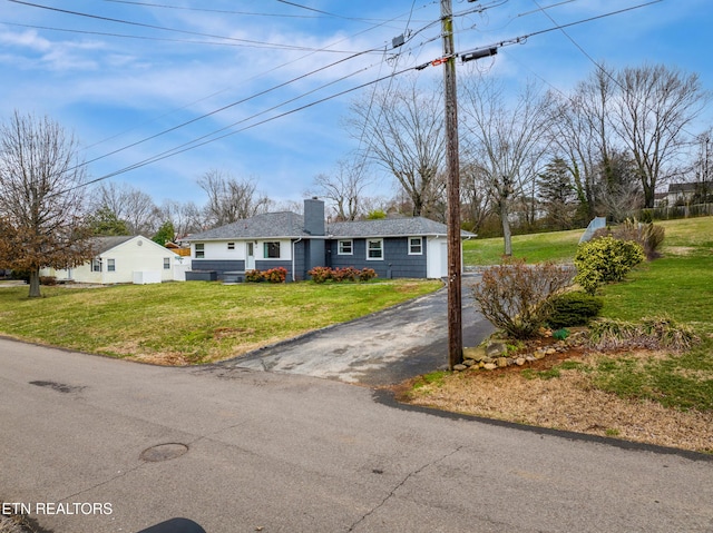 single story home with driveway, a chimney, and a front lawn