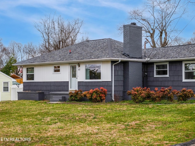 back of property featuring roof with shingles, a lawn, and a chimney