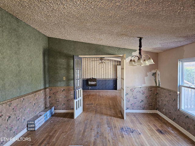 unfurnished dining area featuring a notable chandelier, wallpapered walls, wood-type flooring, and a wainscoted wall