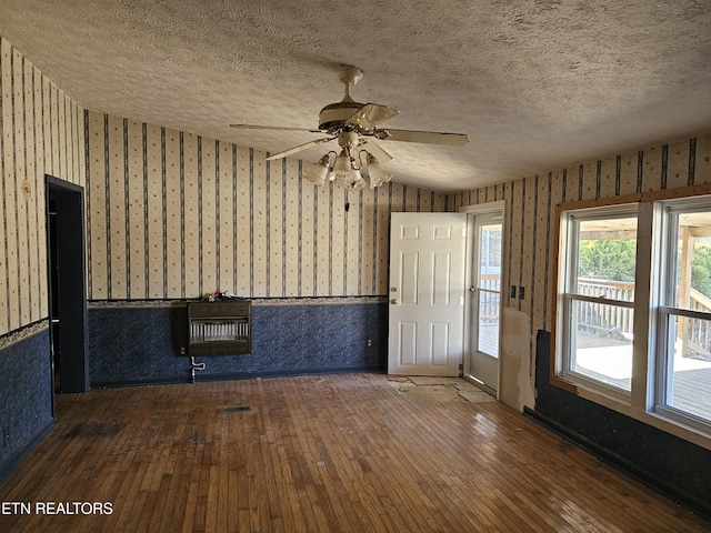 empty room featuring heating unit, wallpapered walls, a textured ceiling, and a wainscoted wall