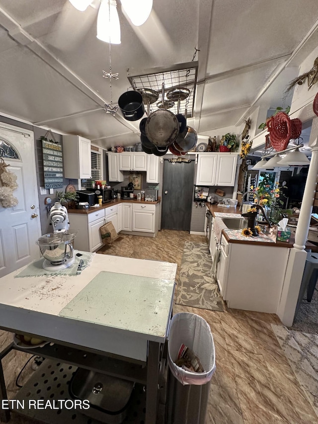 kitchen featuring lofted ceiling, fridge, white cabinets, and a sink